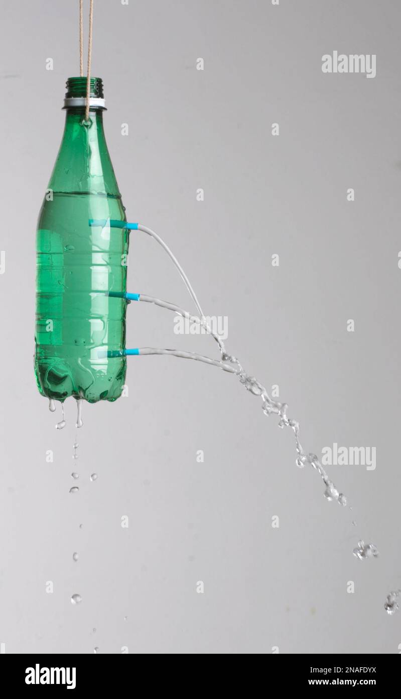 Bottiglia verde penzolante dal filo con tre fori dove l'acqua sta versando fuori Foto Stock