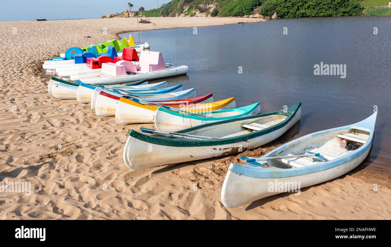 Vacanza panoramica destinazione estiva sulla spiaggia fiume estuario laguna con pedalò canoe kayak di diversi colori e forme sulla linea di sabbia acqua vicino Foto Stock