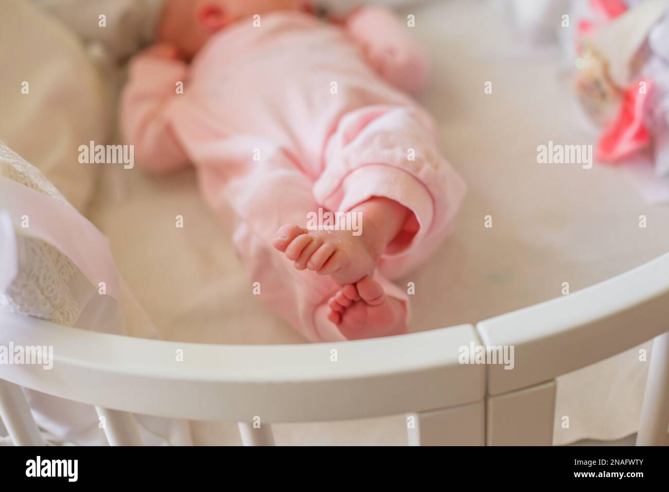 Piccoli piedi per bambini rivestiti in rosa rompero. Piccole dita del neonato. il bambino ha gambe incrociate e si trova nel letto bianco. Foto Stock