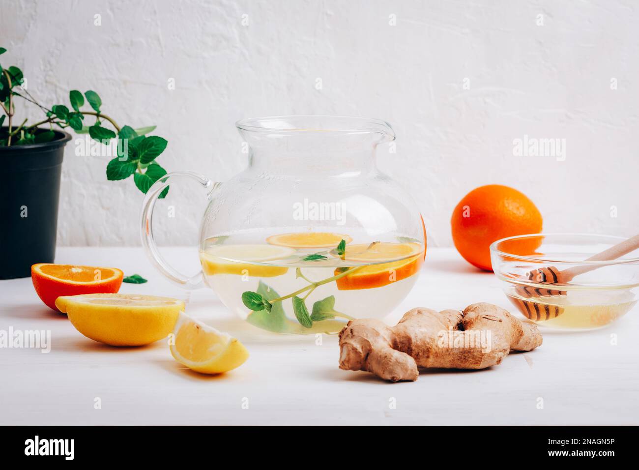 Teiera di vetro con tè all'arancia, al limone, allo zenzero e alla menta con ingredienti su sfondo bianco, primo piano. Foto Stock