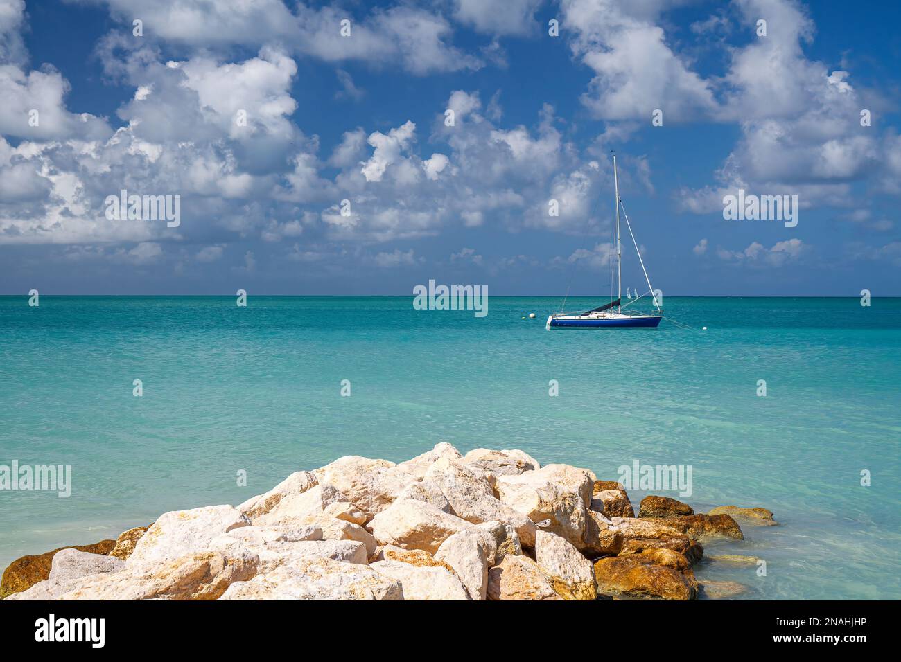 Spiaggia di Antigua Barbuda con molo roccioso e sfondo del paesaggio della barca a vela Foto Stock