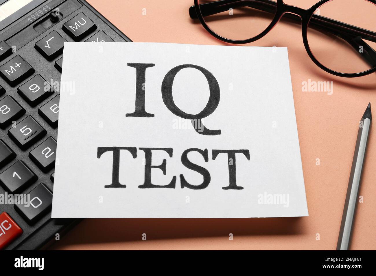 Nota con testo IQ Test, calcolatrice, occhiali e matita su sfondo corallo, primo piano Foto Stock