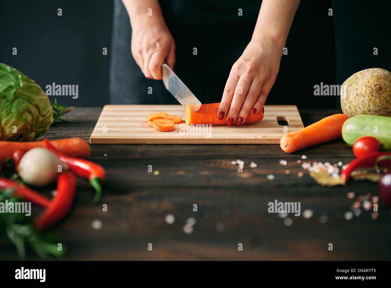 Donna che cucina in cucina a casa. Primo piano delle mani femminili che affettano le carote sul tagliere. Cucina, concetto di alimentazione sana Foto Stock