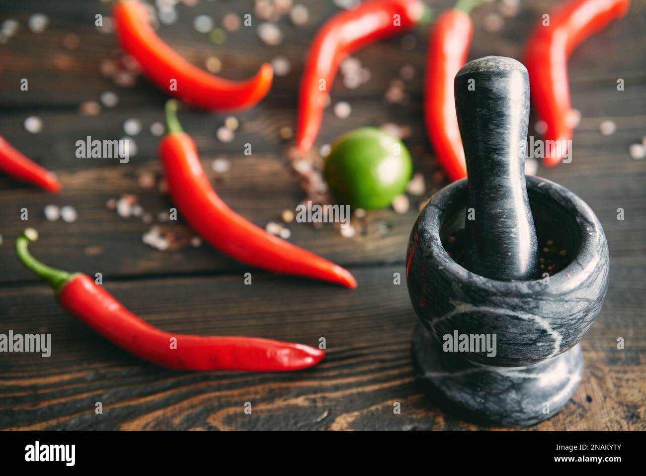 Mortaio in marmo nero con pestello pieno di pepe misto con peperoncino rosso caldo sullo sfondo. Spezie per la cucina, concetto di stile degli alimenti Foto Stock