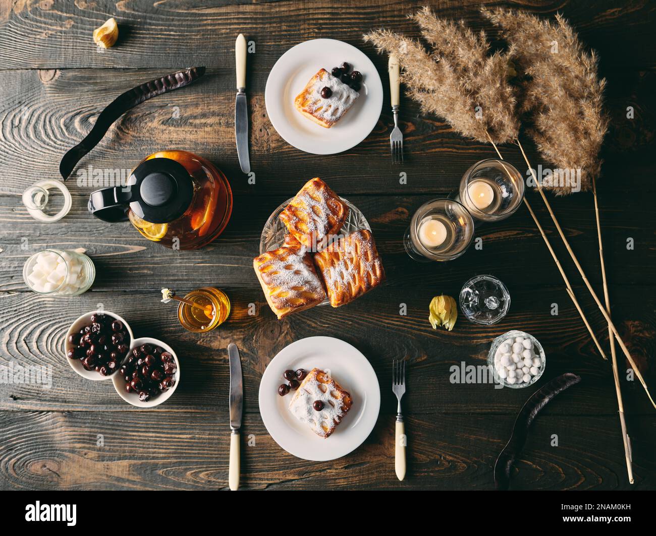 Vista dall'alto del tavolo splendidamente servito decorato in stile rustico con dolci fatti in casa, teiera e candele. Casa accogliente, tempo del tè, cena romantica, cibo Foto Stock