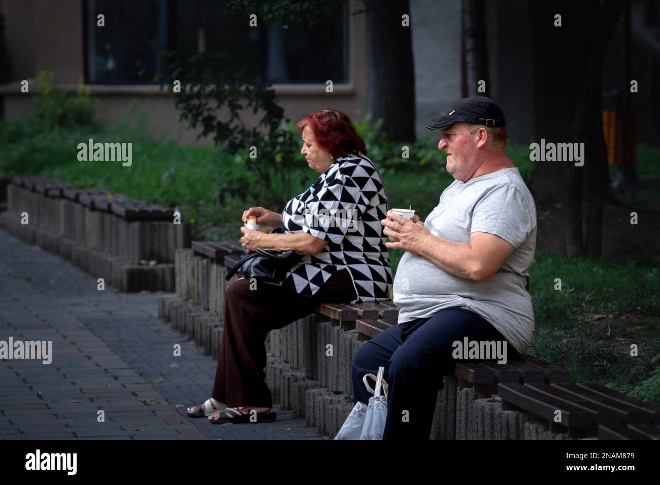 Immagine di due anziani, anziani e donne, seduti, rilassandosi e mangiando cibo e caffè da asporto per le strade di Caransebes, Romania. Foto Stock
