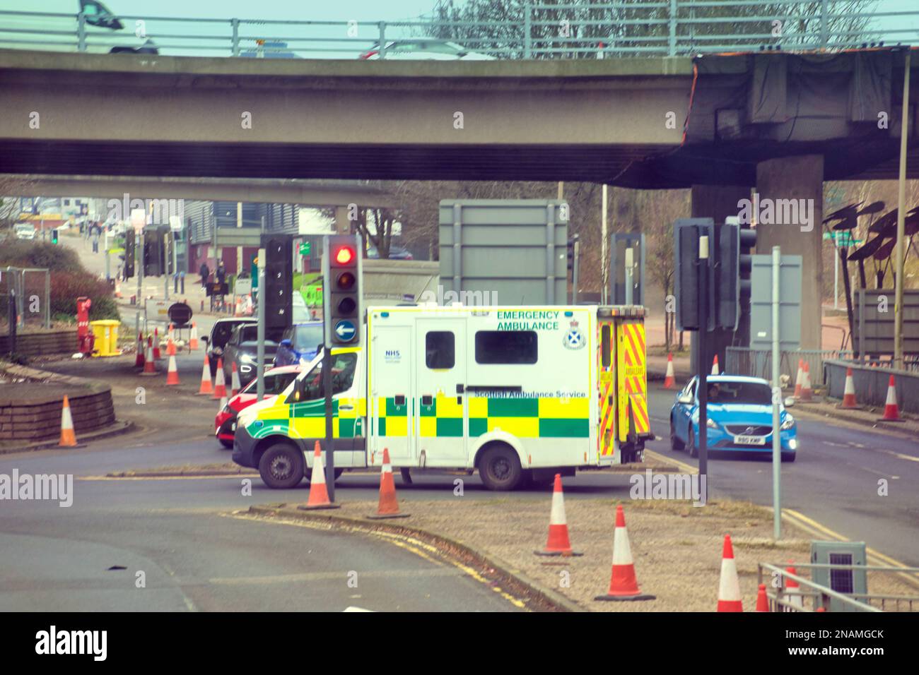 Ambulanza di emergenza nel traffico su una chiamata che attraversa la strada cittadina ai semafori sotto la M8 Foto Stock