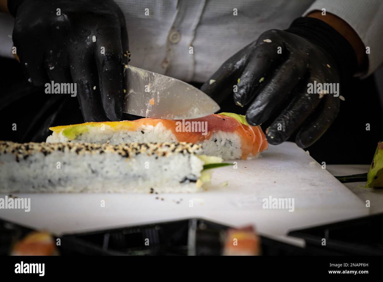 Foto di sushi preparati e confezionati per essere consegnati, con un focus sulle mani di uno chef sushi. Foto Stock