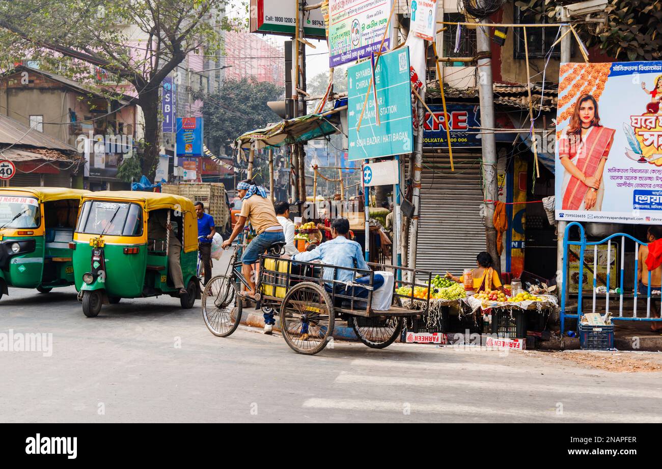 Scena di strada in Kanna, Shyam Bazar, Kolkata suburbana, Bengala Occidentale, India con carrello triciclo e autorickshaws (tuktuks) nella strada Foto Stock
