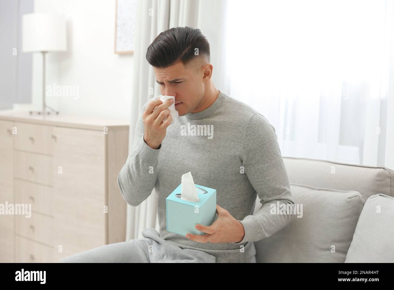 Malato uomo con scatola di carta fazzoletti sul divano a casa Foto Stock
