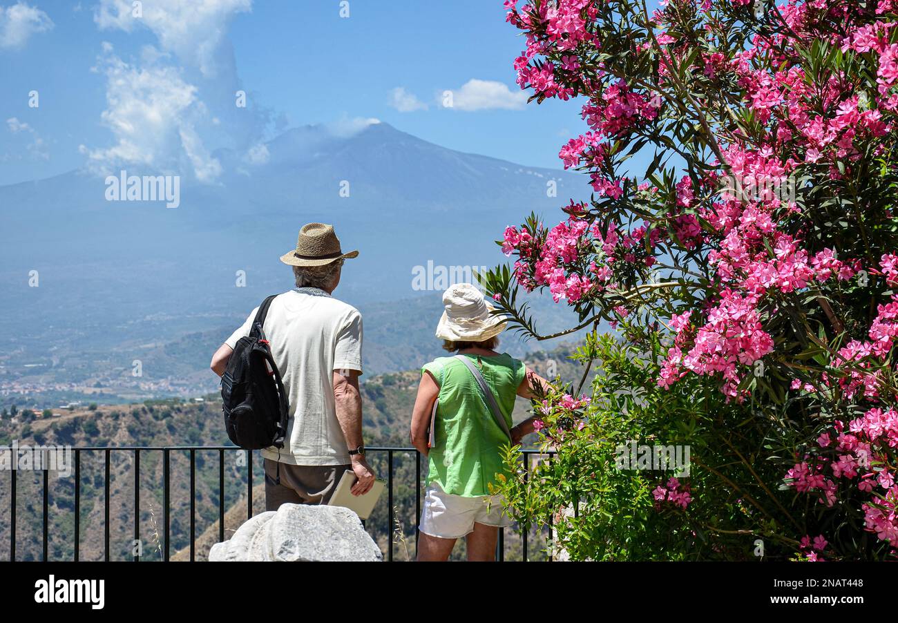 Coppia anziana che guarda l'Etna da un bellissimo punto di vista fiorito nell'antico teatro di Taormina, Sicilia, Italia. Foto Stock