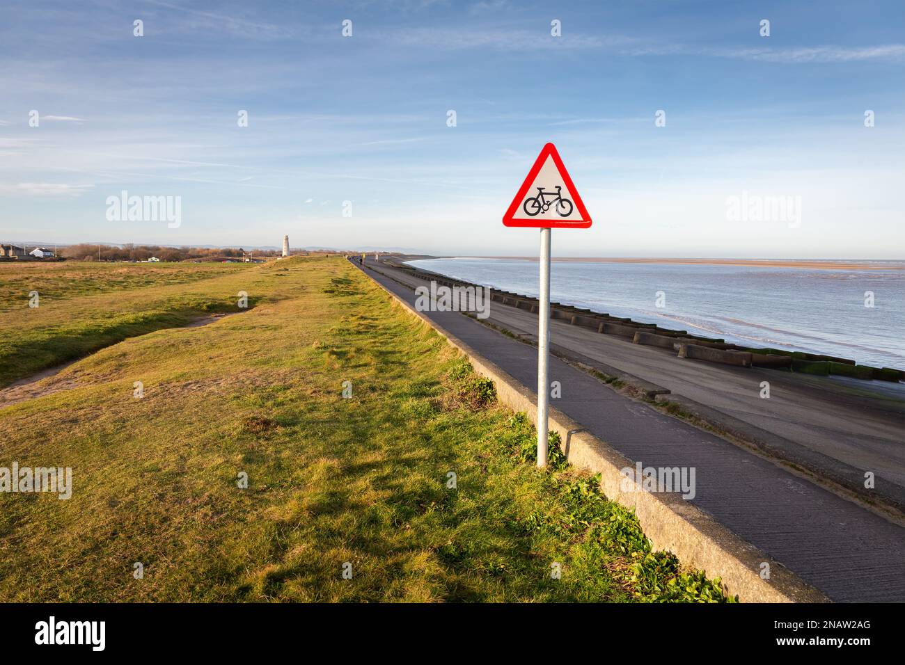 Wallasey, Regno Unito: Pista ciclabile che precede segnale triangolare di avvertimento sull'argine costiero, North Wirral Coastal Park. Foto Stock
