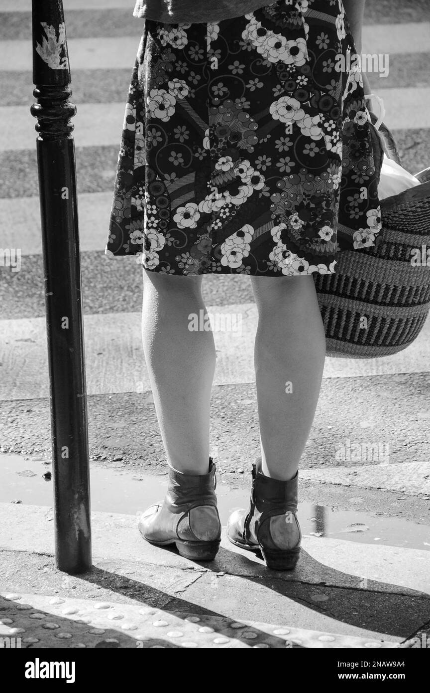 Donna che indossa gonna floreale e con cestino per lo shopping a mano che attraversa la strada parigina. Parigi, Francia. Atmosfera primaverile in aria. Foto in bianco e nero Foto Stock