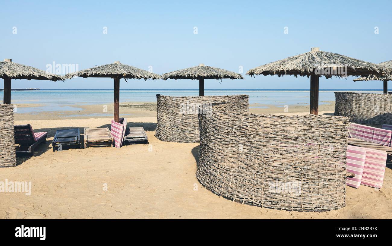 Spiaggia tropicale con ombrelloni in legno, lettini e parabrezza, tonificante. Foto Stock