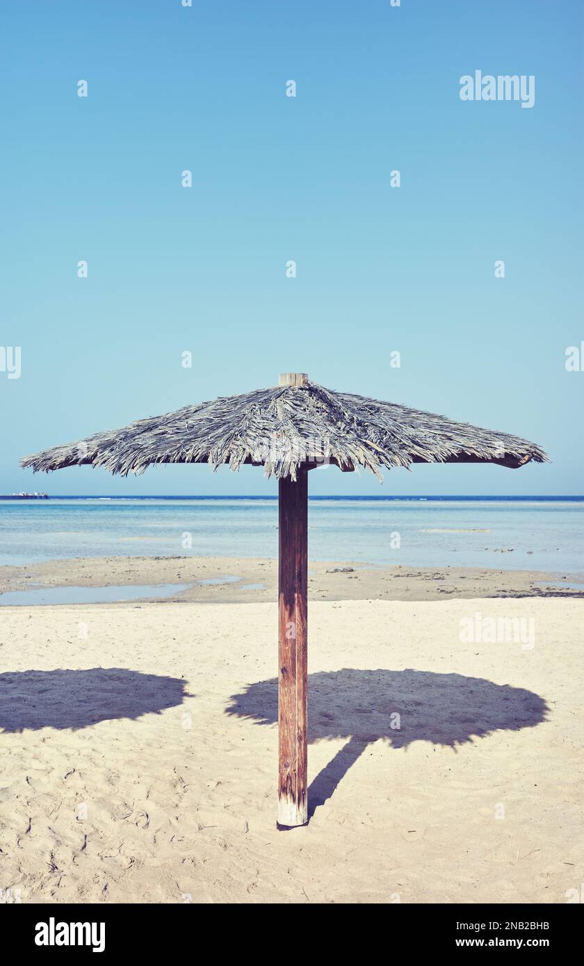 Spiaggia tropicale con ombrellone in legno, tonificazione cromatica applicata, focalizzazione selettiva. Foto Stock