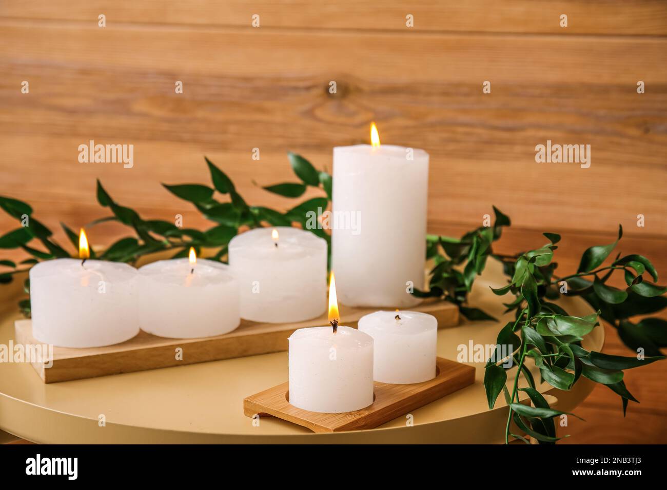 Candele brucianti con rami di pianta su tavolo vicino a muro di legno, primo piano Foto Stock