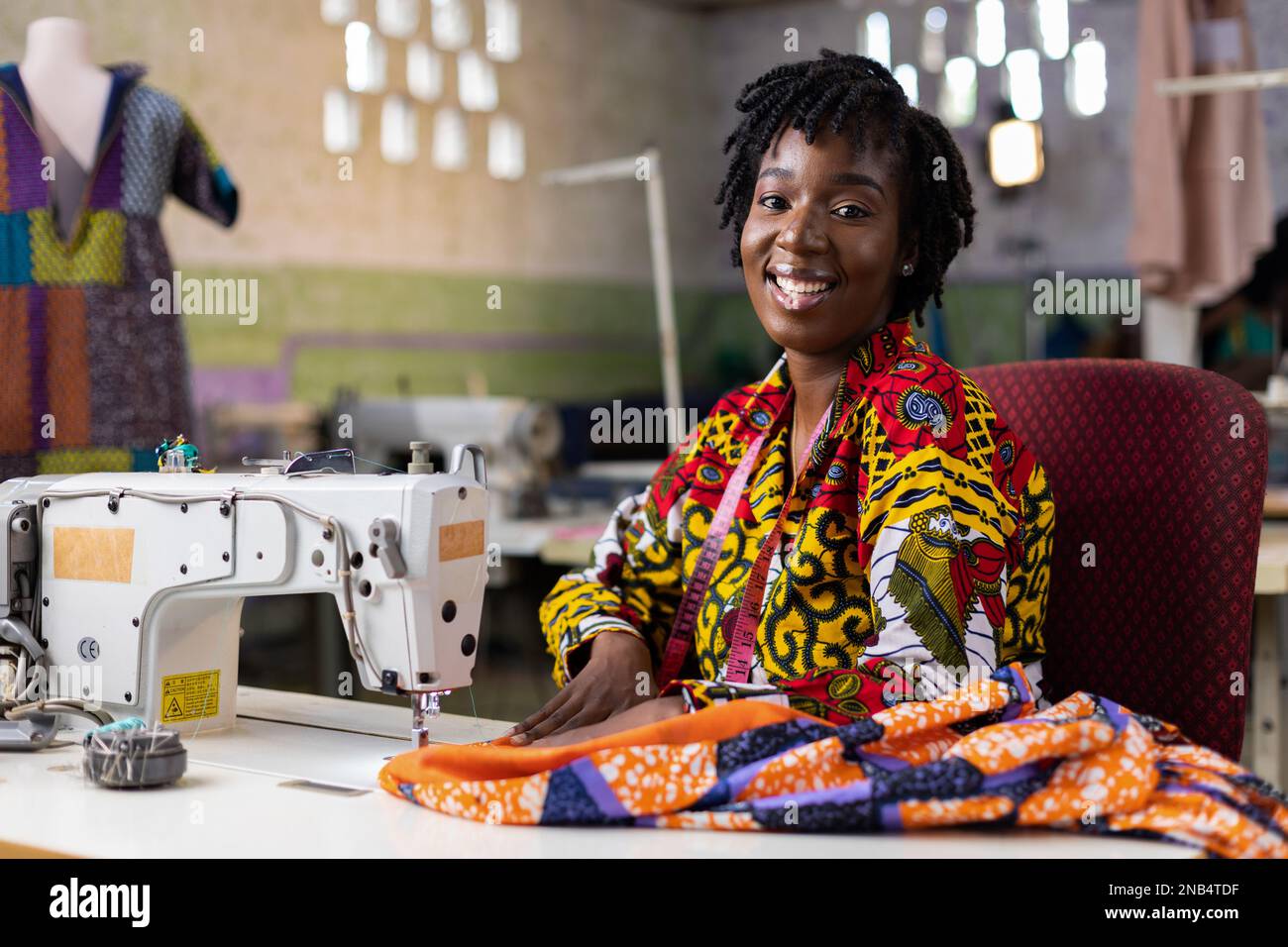 Donna africana imprenditore dresssaker con i capelli locs lavorando nel suo studio di design della moda con una macchina elettrica. Foto Stock