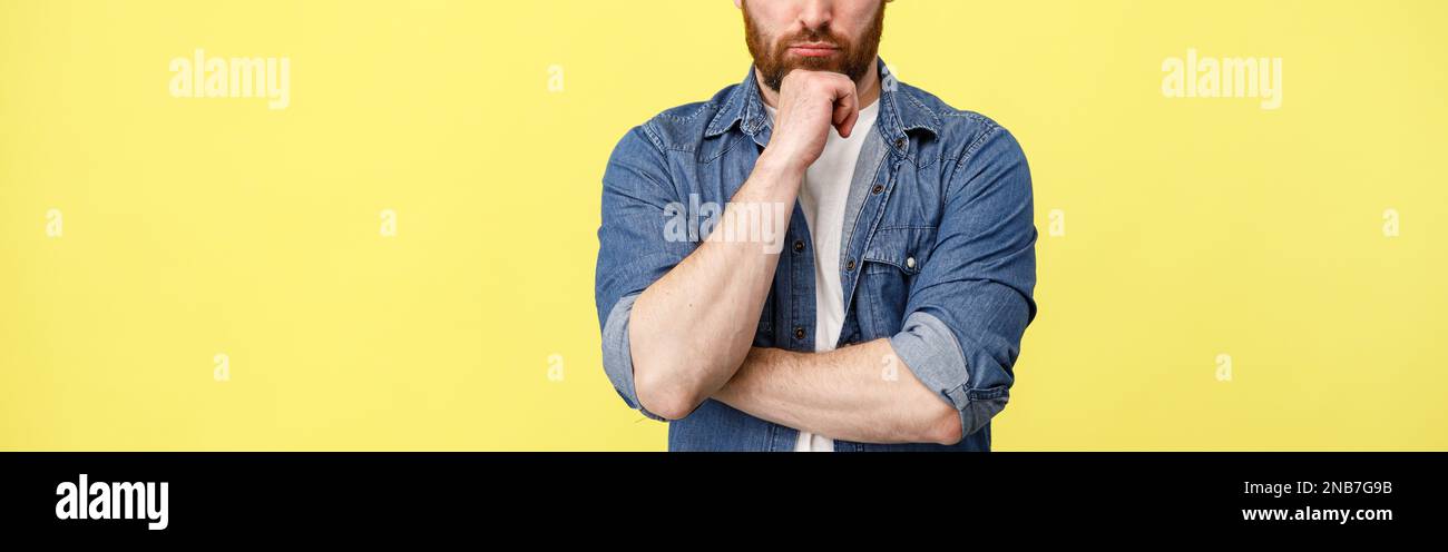L'uomo serio tiene la mano a destra vicino la barba sullo sfondo giallo Foto Stock