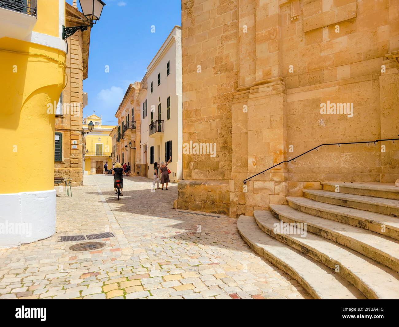 Una donna passa in bicicletta davanti alla cattedrale di Ciutadella de Menorca nel centro medievale della città, sull'isola delle Baleari in estate. Foto Stock