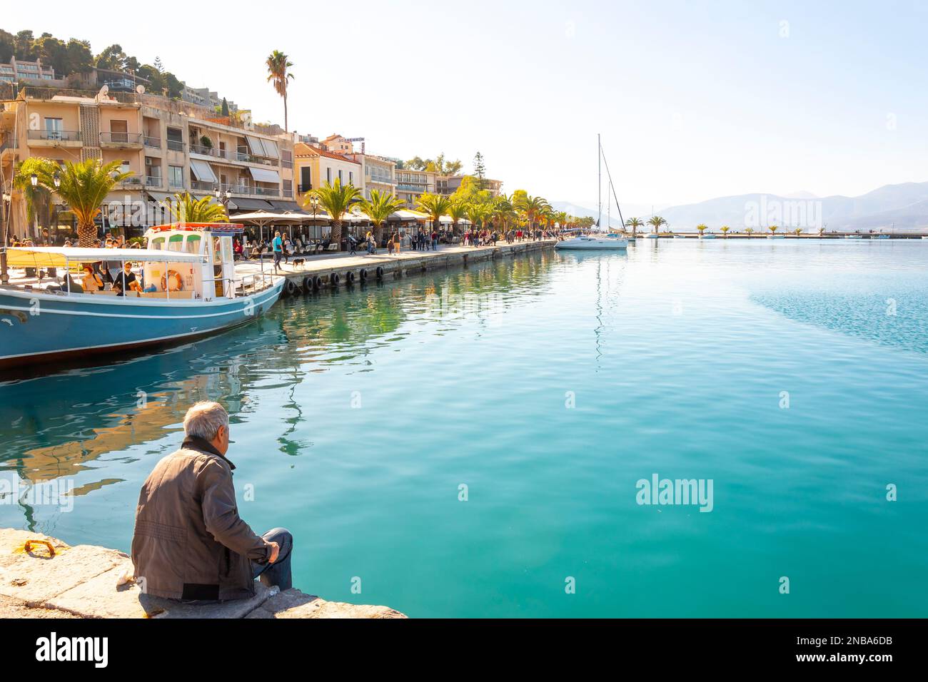 Un pescatore greco guarda i turisti dal porto nel pittoresco villaggio sul mare di Nafplio, in Grecia. Foto Stock