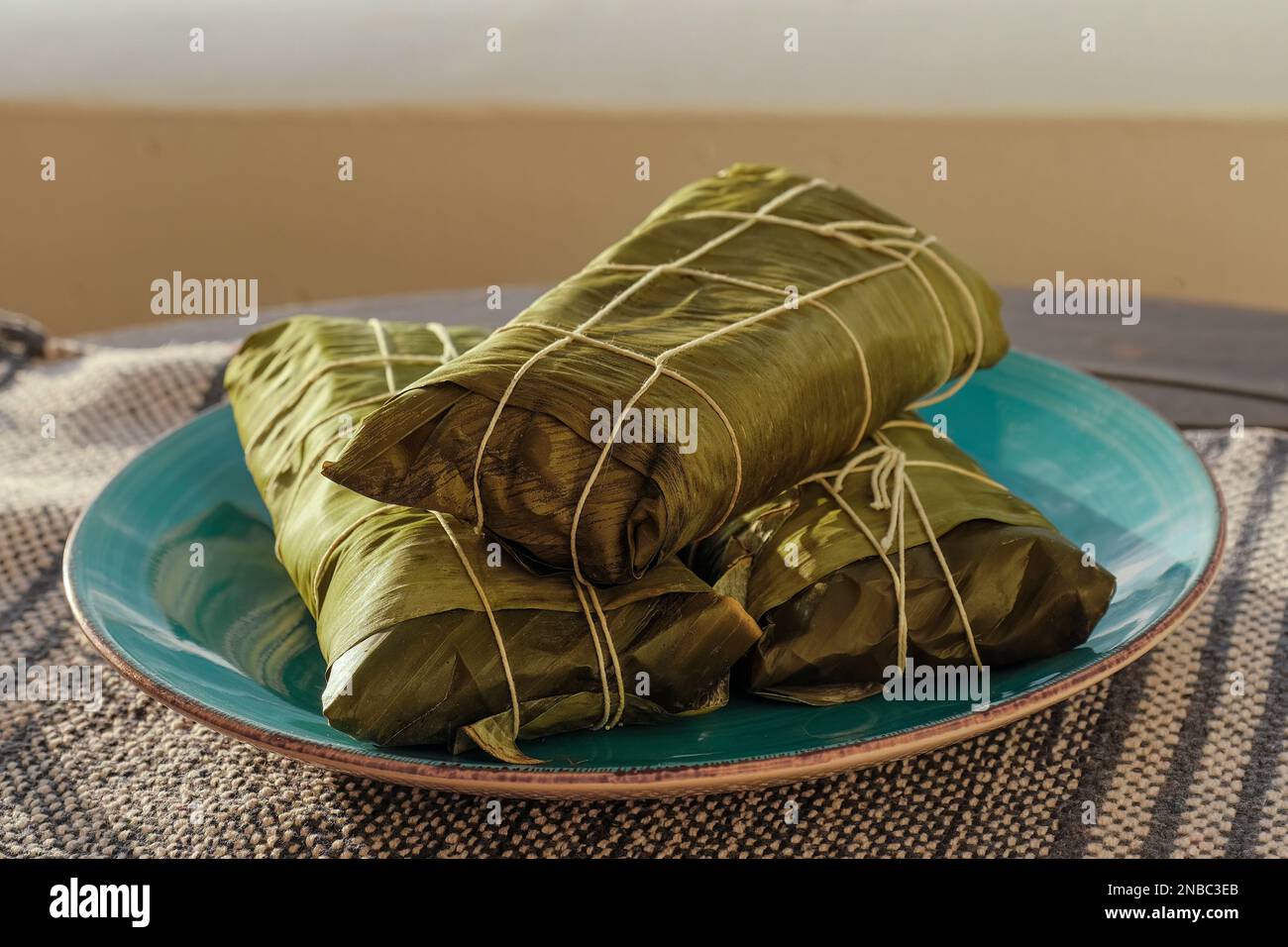 Avvolto Hallaca o Tamale su un tavolo rustico e un piatto blu, messicano e venezuelano tradizionale cibo Foto Stock