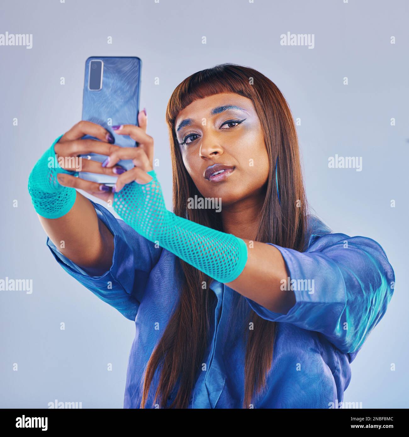 Moda selfie e donna con smartphone e abbigliamento al neon cyberpunk isolato su sfondo blu. Social media futuro e influencer di gen z alla moda Foto stock Alamy