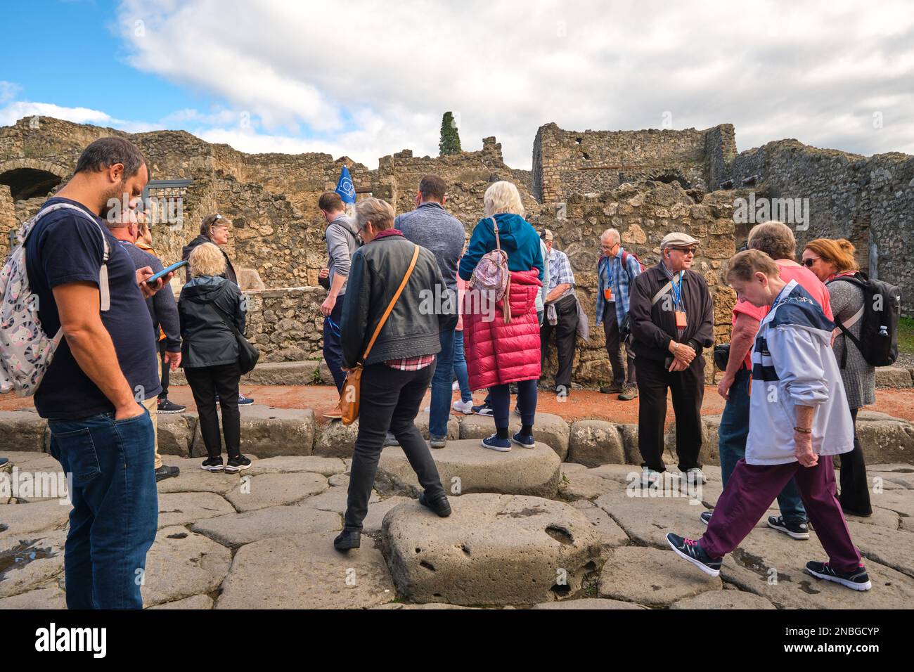 Una vista di un tipico tour di gruppo di visitatori, condotto da qualcuno con una piccola bandiera su un palo. Al Parco Archeologico di Pompei vicino a Napoli, Italia. Foto Stock