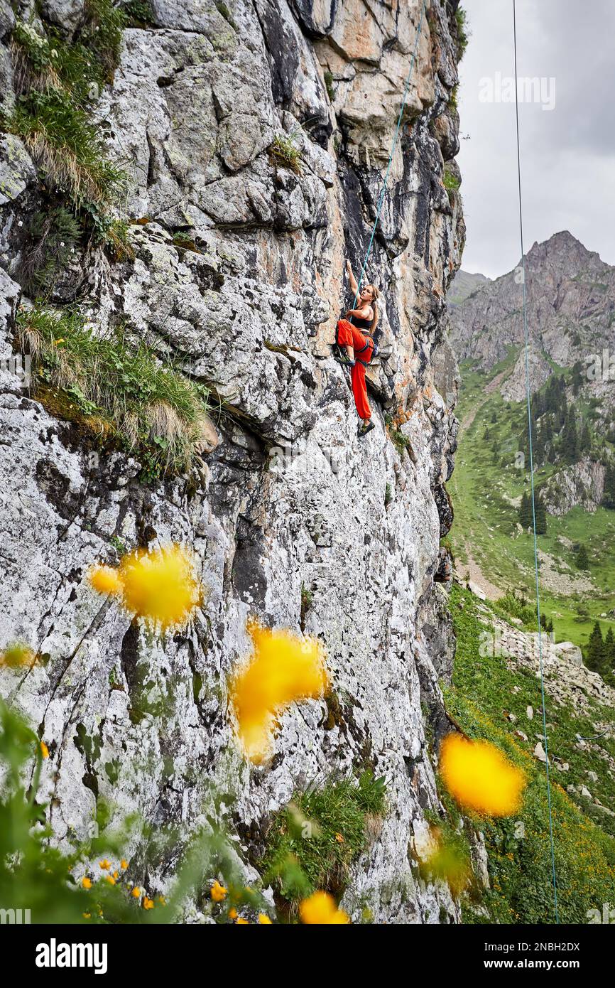 Fit forte donna in costume rosso arrampicata sulla roccia alta verticale sulle montagne Tyan Shan in Kazakhstan Foto Stock
