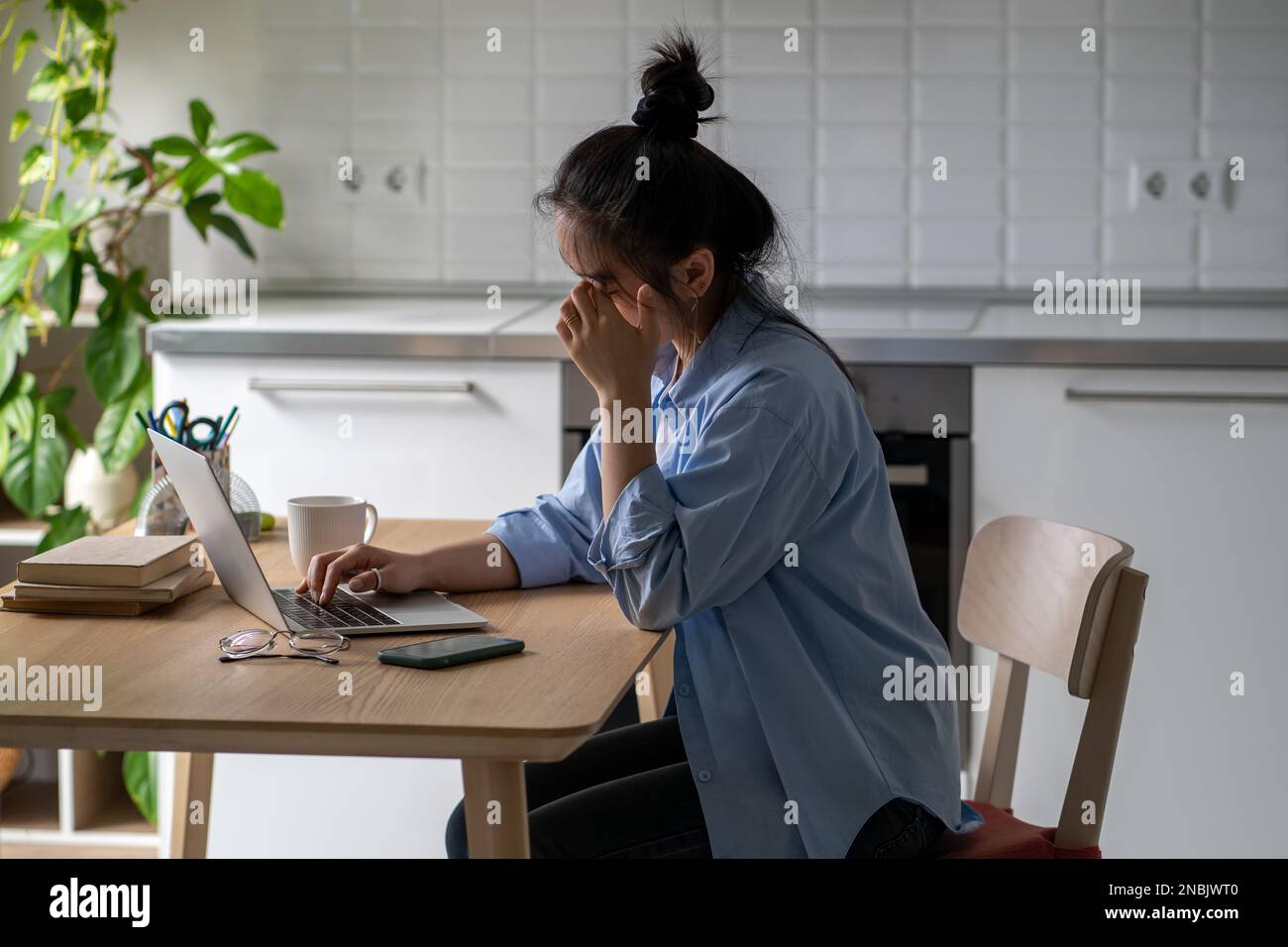 Una giovane donna addormentata si siede alla scrivania sfrega gli occhi stanchi per lavorare online o studiare a lungo con un computer portatile Foto Stock