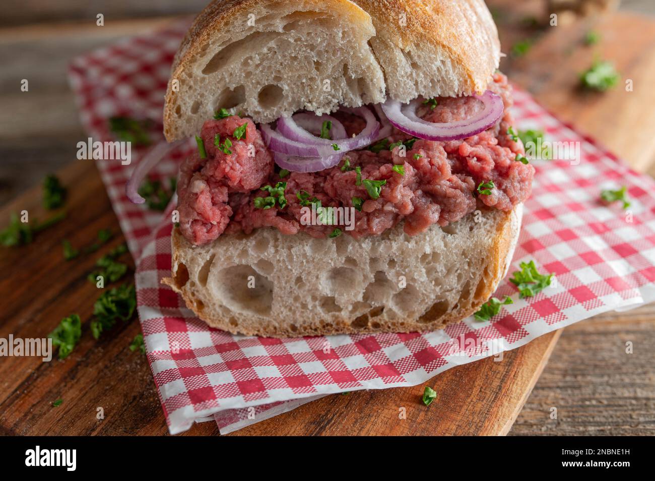 Panino di manzo crudo con cipolle rosse e prezzemolo su una baguette francese. Primo piano e vista frontale Foto Stock