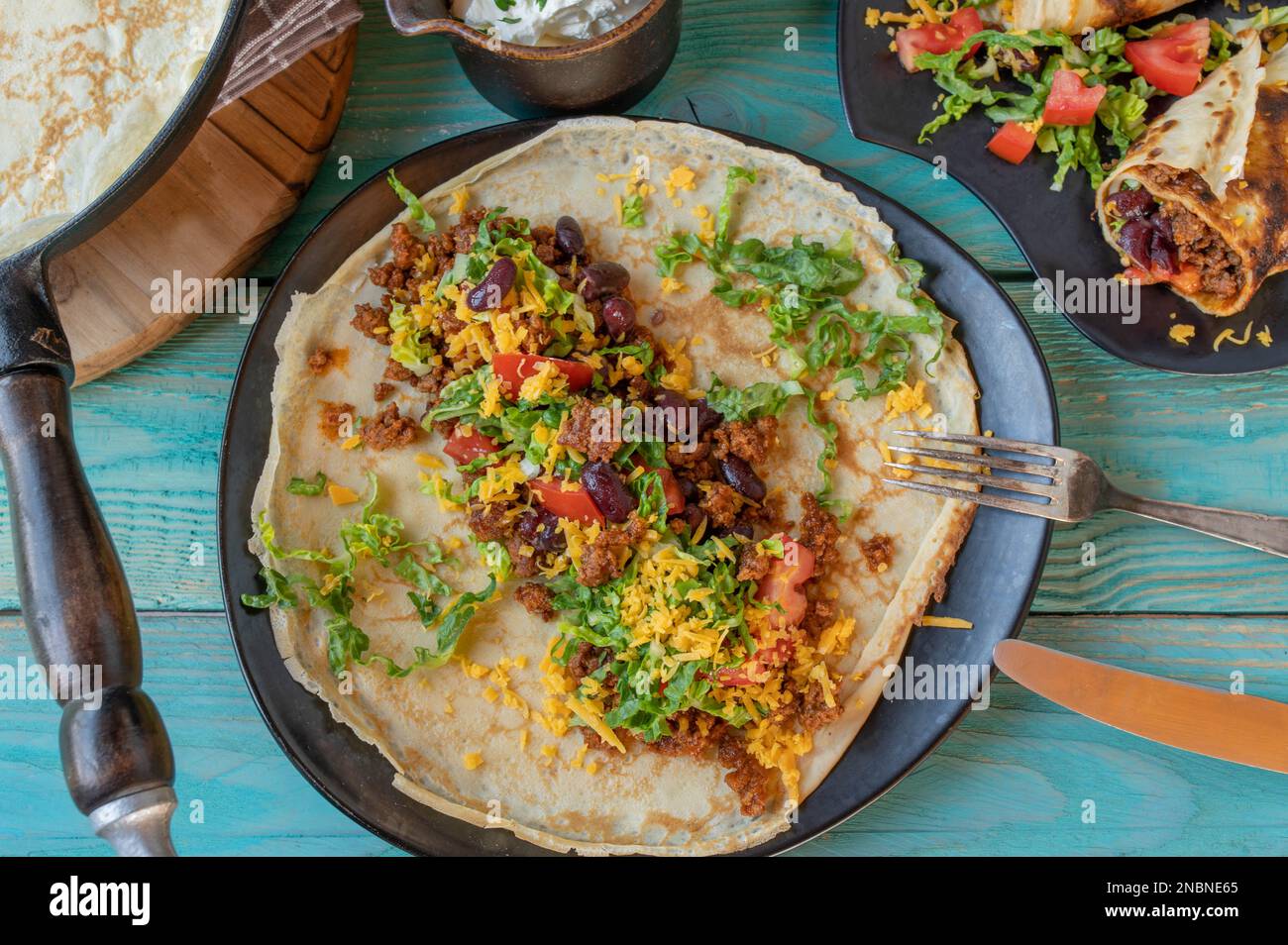 Burrito, crepe o pancake con carne macinata, fagioli rossi, formaggio e verdure serviti su un piatto per cena su un tavolo di legno Foto Stock