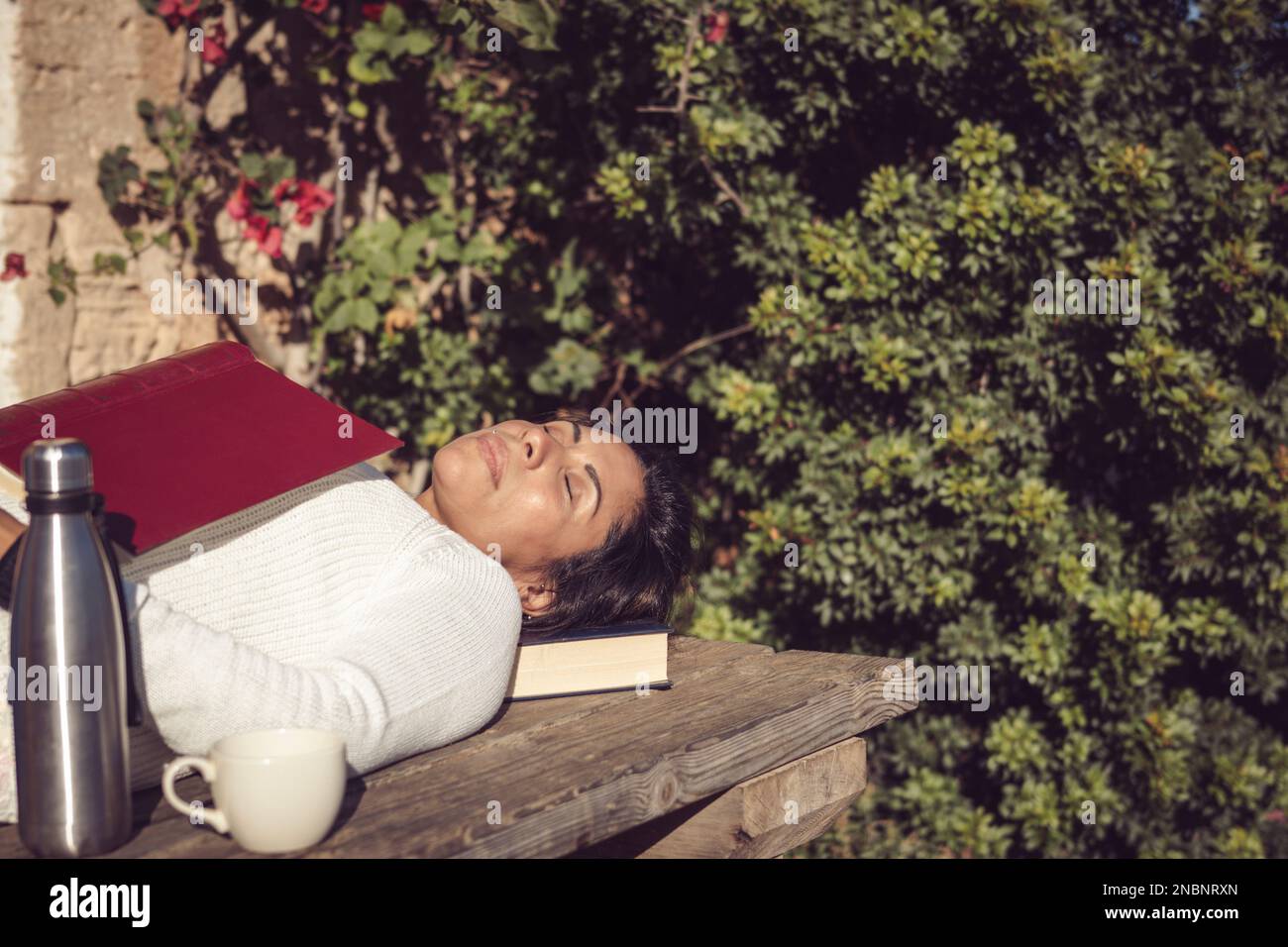 donna latina che dorme al sole con un libro Foto Stock