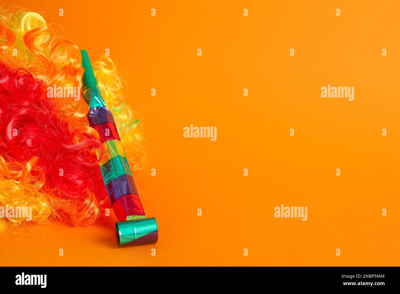 Clown wig e party blower su sfondo arancione, spazio per il testo Foto Stock