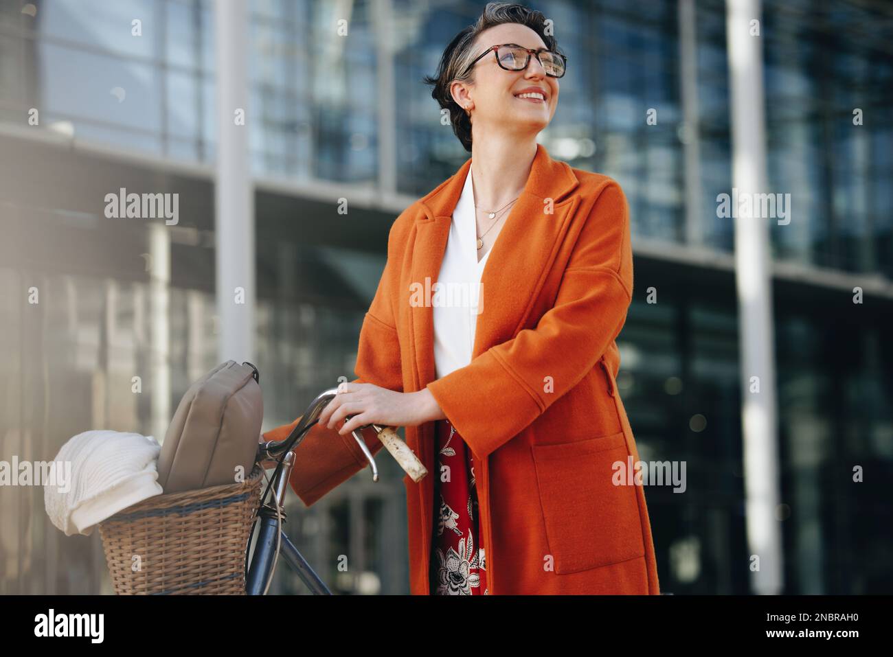 Donna d'affari felice guardando via pensieroso mentre spinge la sua bici nella città. Sorridente donna d'affari matura che si trova in viaggio per lavorare con una bicicletta nel Foto Stock