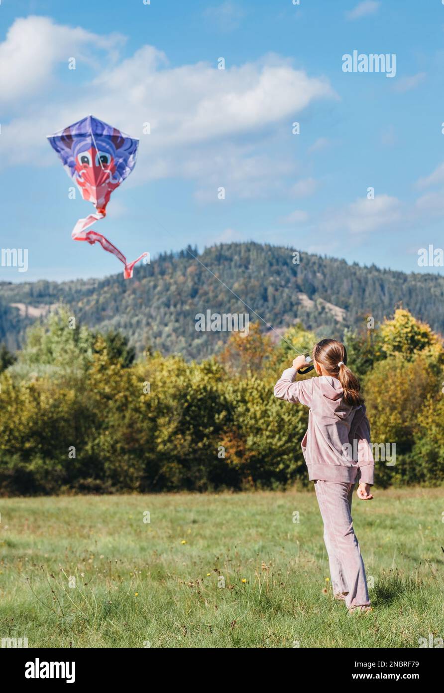 Bambina che vola un aquilone colorato sul prato verde nei campi di montagna. Momenti felici di infanzia o all'aperto spendendo tempo idea immagine. Foto Stock