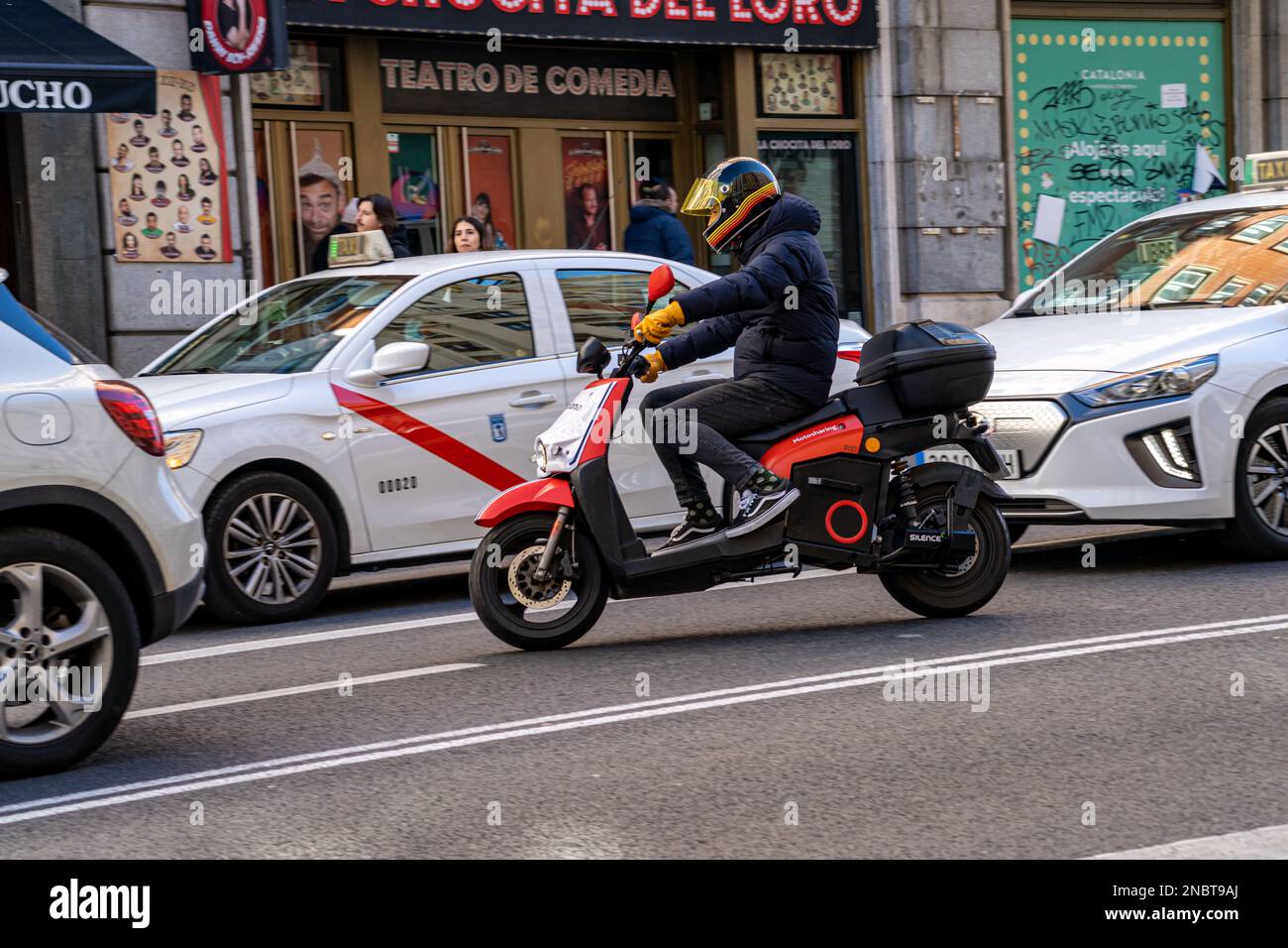 Moto elettrico della società acciona in affitto al minuto guidato lungo la gran via strada a madrid tra diverse auto e taxi. Foto Stock