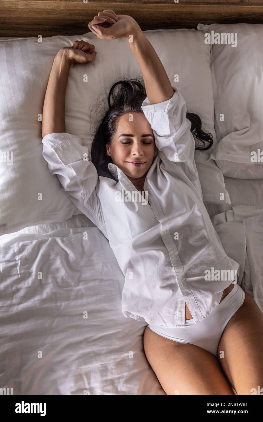 Una giovane donna si sveglia nel letto della sua camera da letto, allunga le braccia e le spalle. Foto Stock