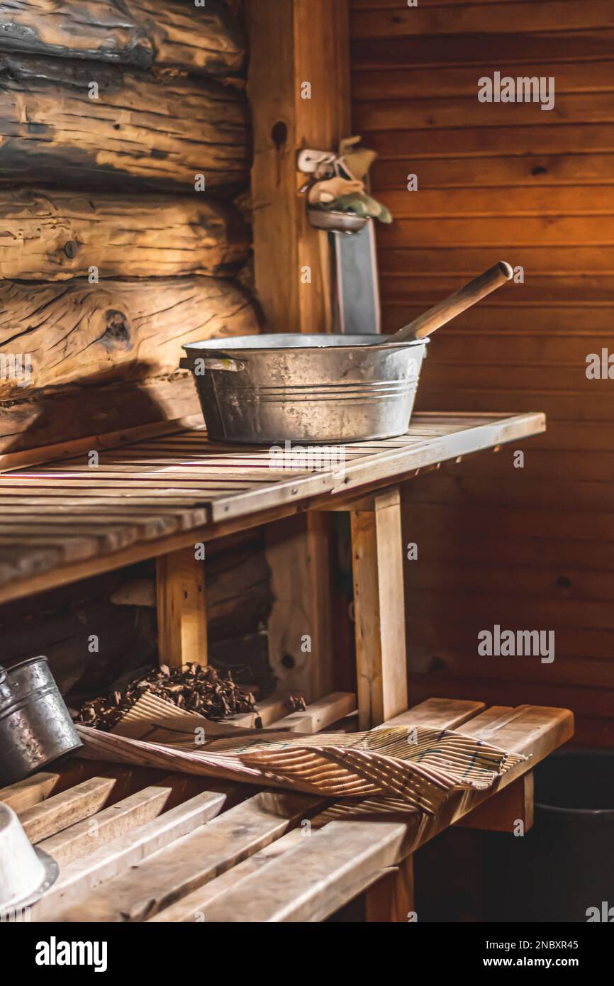 Interno di una tradizionale sauna in legno con secchio e mestolo in metallo posti su una panca in legno. Atmosfera accogliente e rustica tipica della Scandinavia, del Baltico Foto Stock