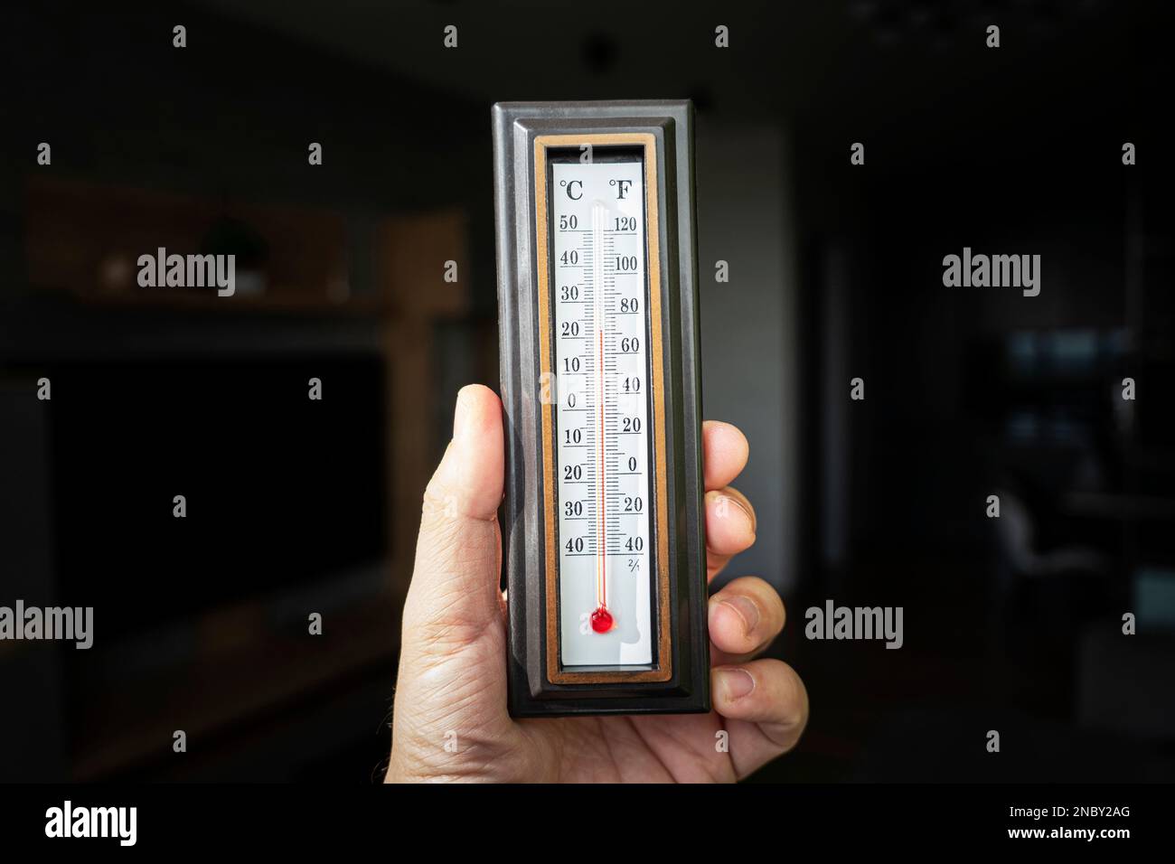 la mano con un termometro a mercurio in plastica mostra la temperatura dell'ambiente. Riscaldamento potente in Russia. 22 gradi Celsius è la norma per la temperatura Foto Stock