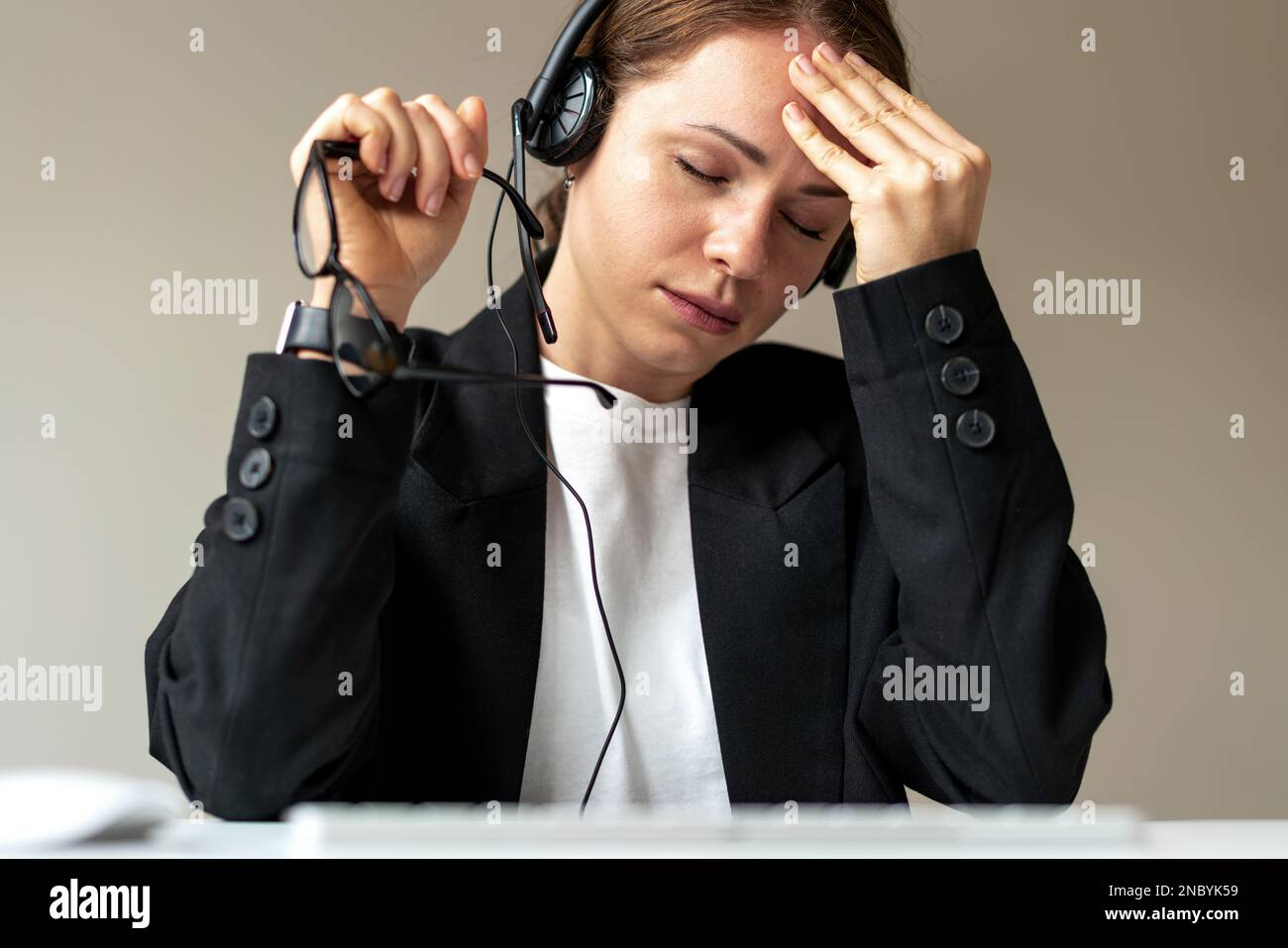 Esausta giovane donna consulente del call center che ha dura giornata sul lavoro, malattia mentale, mal di testa, affaticamento. Foto Stock