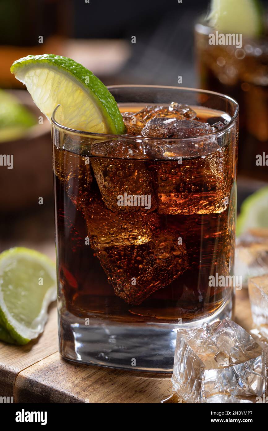 Cocktail al rum e alla cola con lime e ghiaccio a fette su un asse di legno Foto Stock