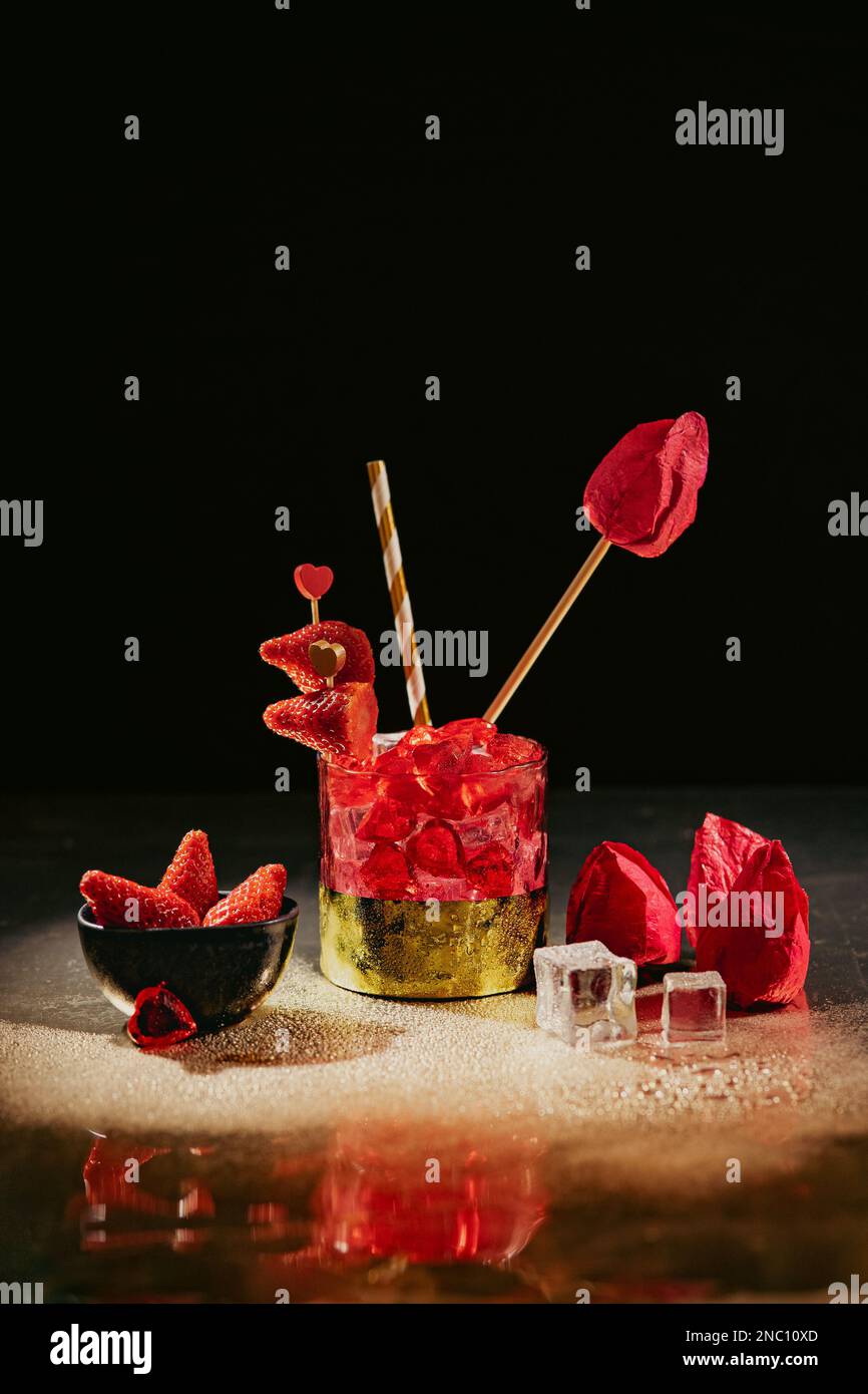 un bicchiere rosso e oro con drink/cocktail di san valentino, fragole e fondo scuro Foto Stock