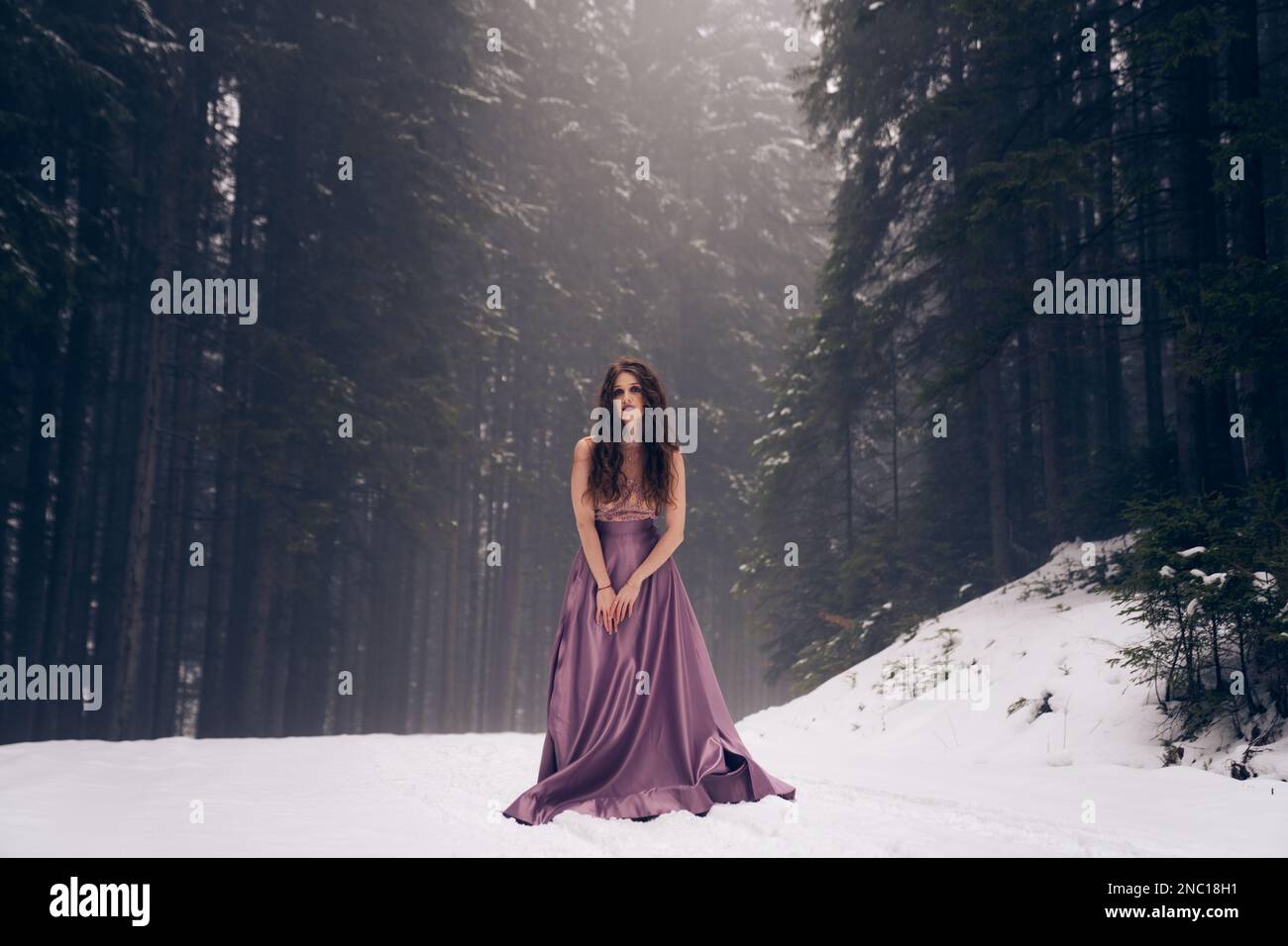 Una donna in un abito di raso viola contro il paesaggio invernale, foresta innevata sentiero Foto Stock