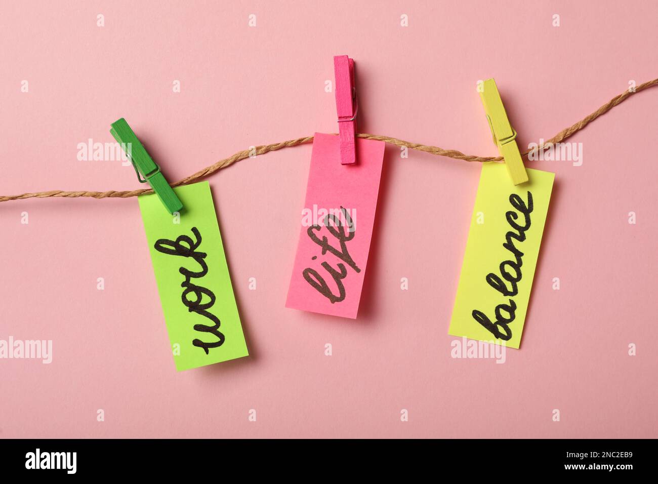 Pezzi di carta con parole lavoro, vita, equilibrio appeso su corda contro sfondo rosa, piatto Foto Stock