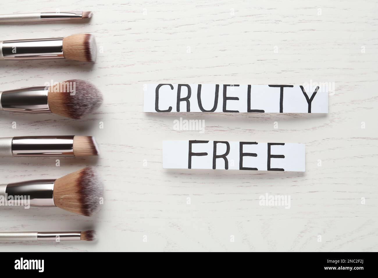 Carte con testo crudeltà Gratis e pennelli da trucco su tavolo di legno bianco, piatto. Arrestare i test sugli animali Foto Stock