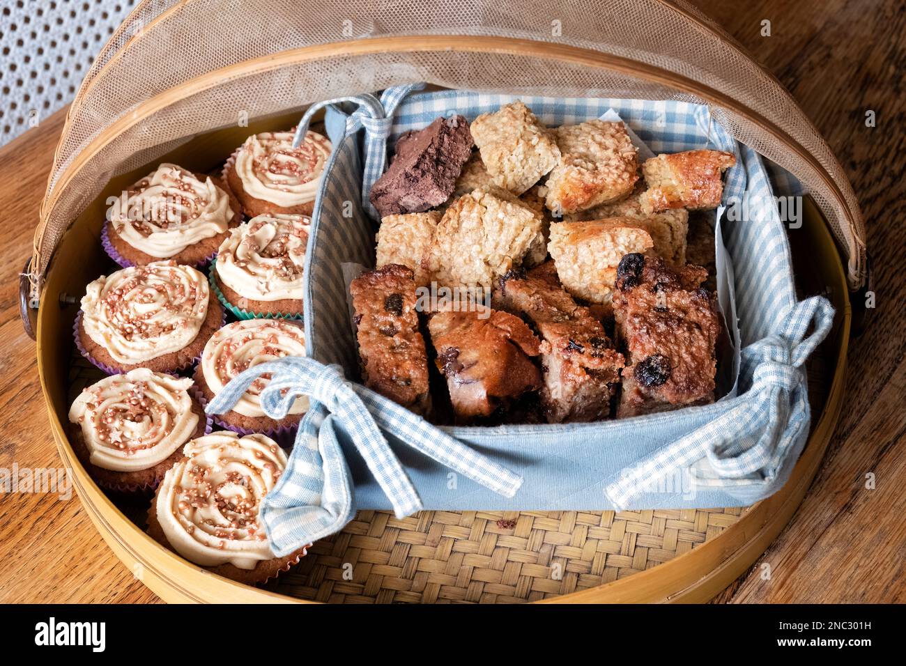 Un assortimento di dolci gustosi tra cui torte, flapjacks e fette di pane budino. Tutti sono esposti in una coperta di cibo di bambù Foto Stock