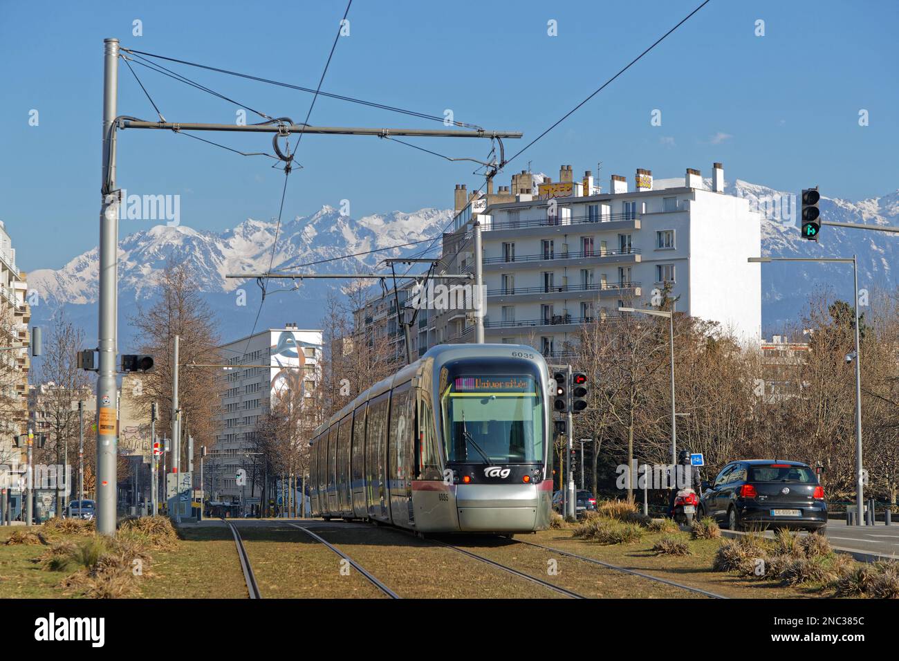 GRENOBLE, FRANCIA, 8 febbraio 2023 : le linee del tram attraversano il centro della città con le montagne innevate della catena Belledonne sullo sfondo. Foto Stock