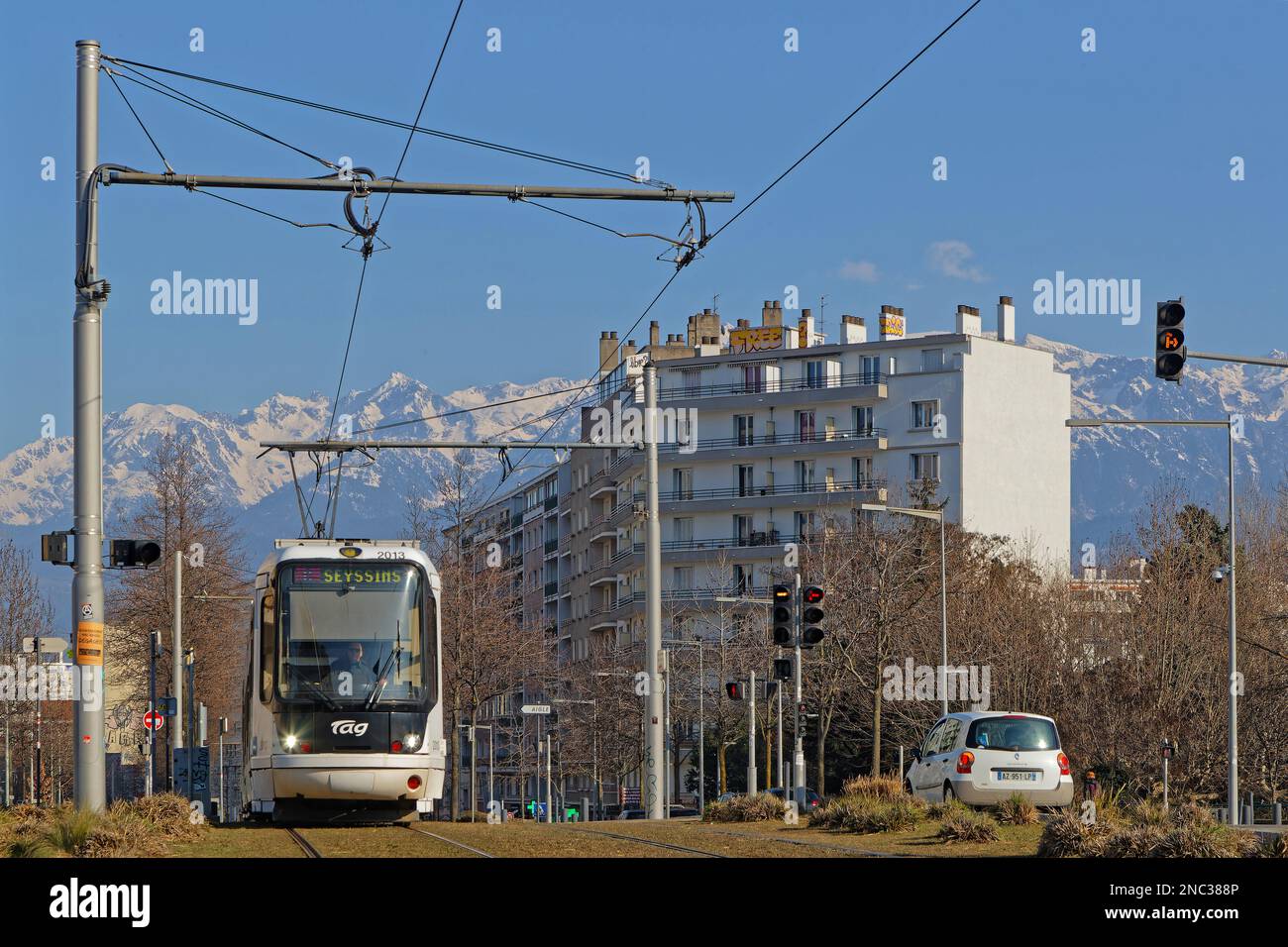 GRENOBLE, FRANCIA, 8 febbraio 2023 : le linee del tram attraversano il centro della città con le montagne innevate della catena Belledonne sullo sfondo. Foto Stock