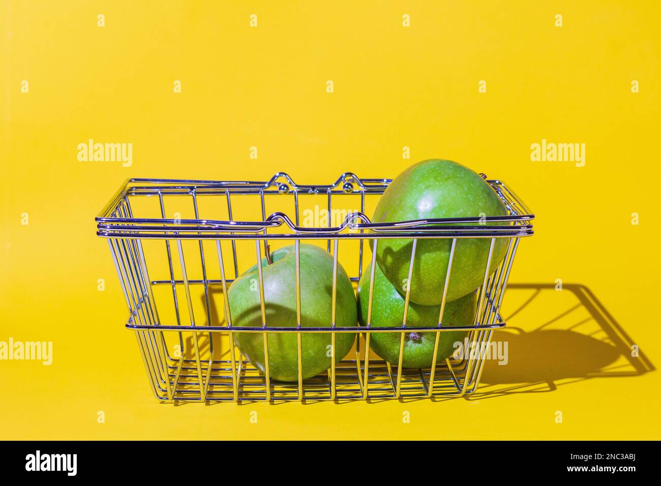 carrello con mele, frutta per il cibo, carrello supermercato, diversi oggetti, verde rotondo, griglia di metallo, si trova sulla superficie dello sfondo giallo. Foto Stock