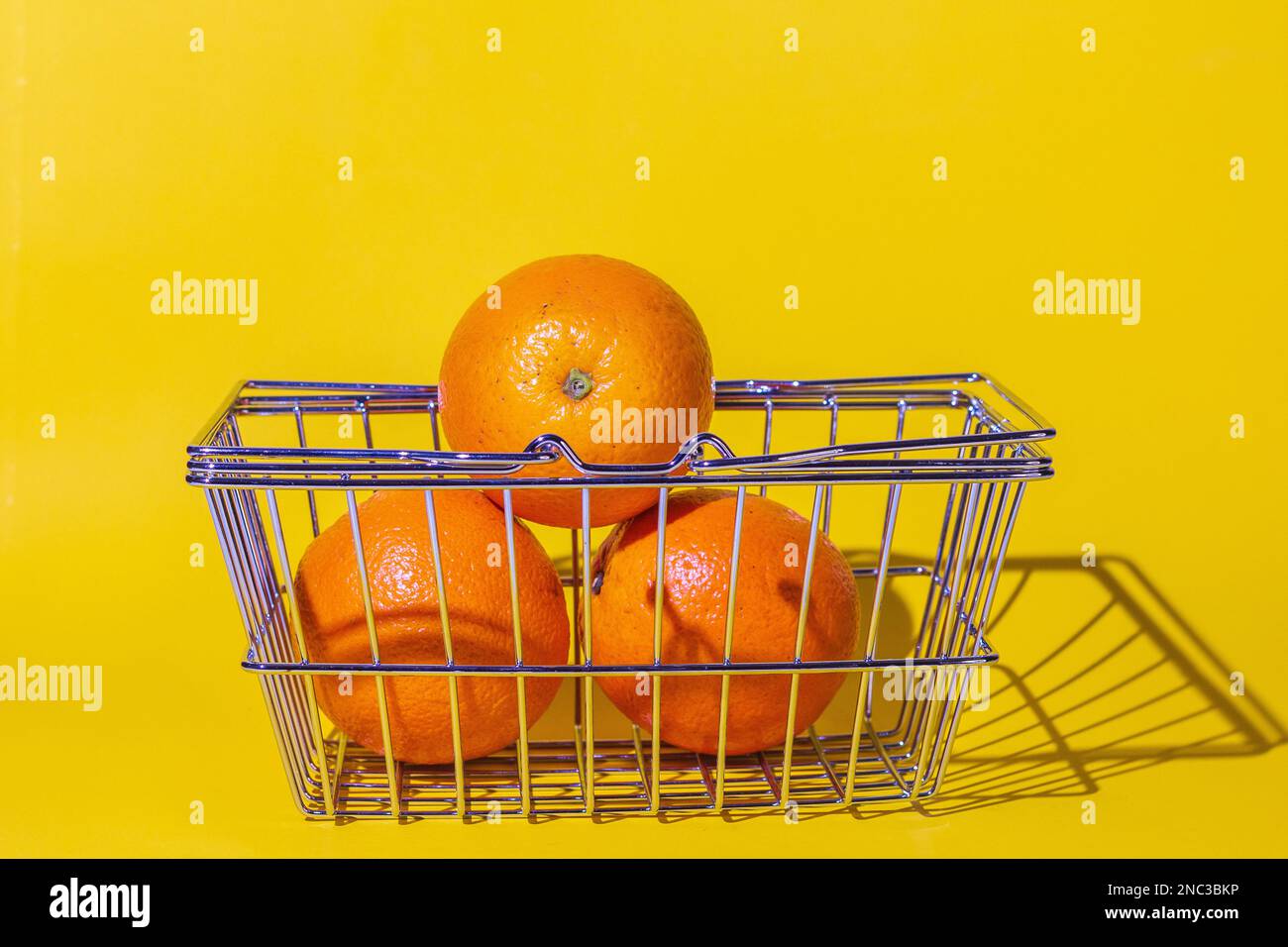 carrello con arance, frutta per il cibo, carrello supermercato, diversi oggetti, arancio rotondo, griglia di metallo, si trova sulla superficie del backgroun giallo Foto Stock